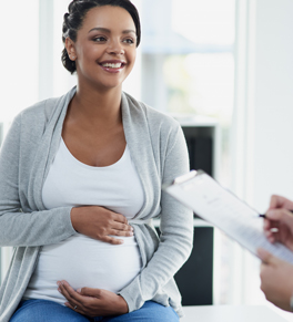 a pregnant woman sits on the table in her doctor's office, who is taking notes